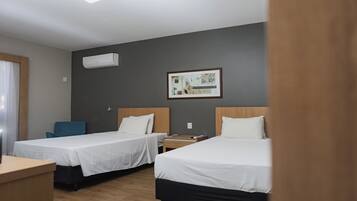 A hotel room with two beds, a desk, a chair, a painting on the wall, and an air conditioning unit.