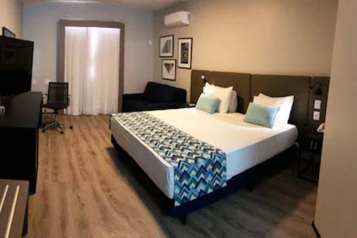 A hotel room with a bed, a desk, a chair, a TV, and a door.