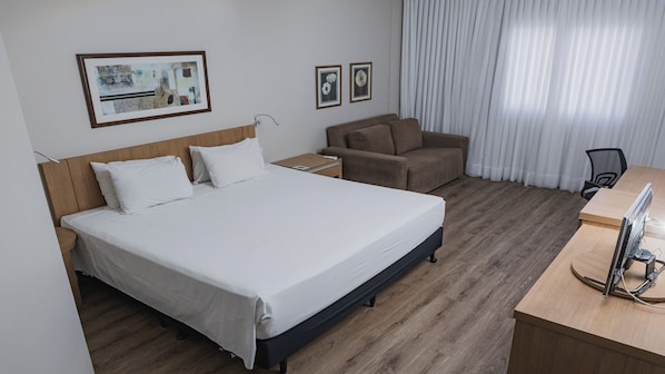 A hotel room with a bed, a desk, a chair, and a television.