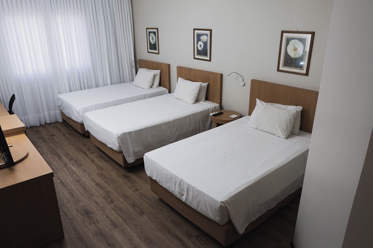 A hotel room with three single beds, a wooden desk, and a TV.