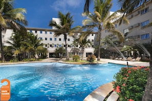 A swimming pool surrounded by palm trees and a building with multiple balconies.