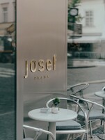 Um café chamado 'Josef', com design moderno, com mesas redondas e cadeiras de metal.