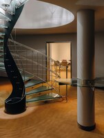 A modern interior with a spiral staircase, a glass table, and a large cylindrical column.