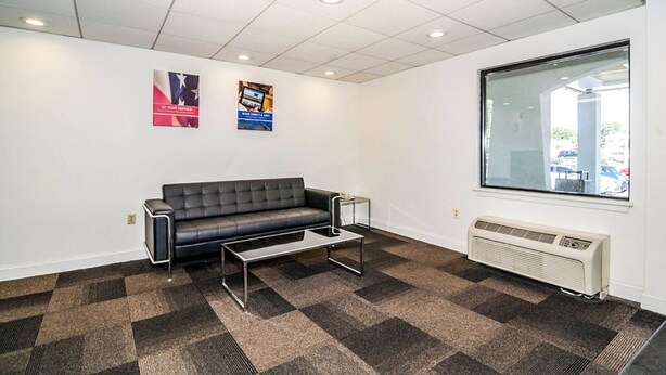 A modern office space with a black leather couch, a glass coffee table, and a large window providing a view of the outside. - Motel 6 Newark, DE (Newark)