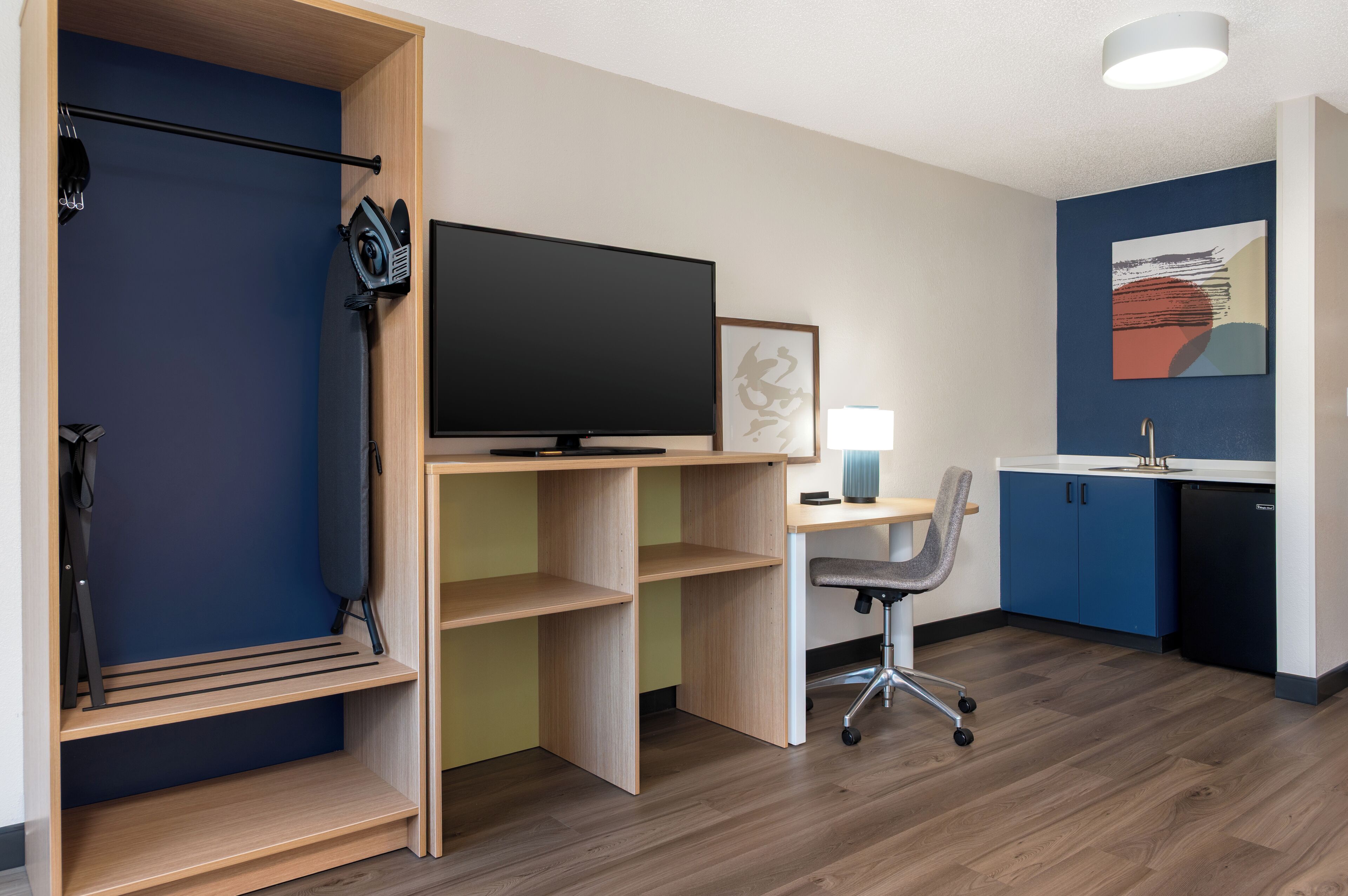 A compact room with a TV, desk, chair, and storage shelves.