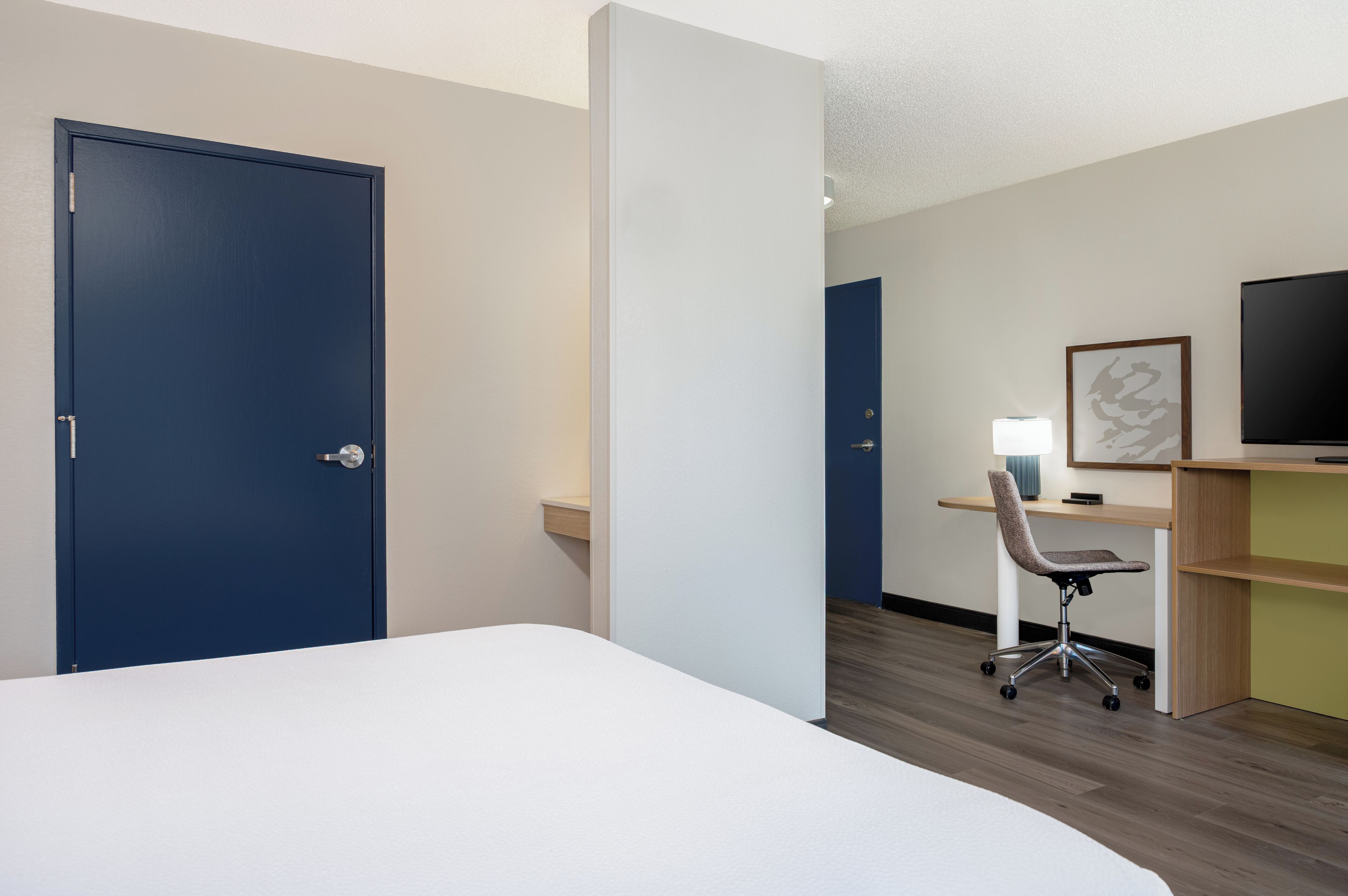 Une chambre d’hôtel avec un lit, un bureau avec une chaise, une télévision et une porte.