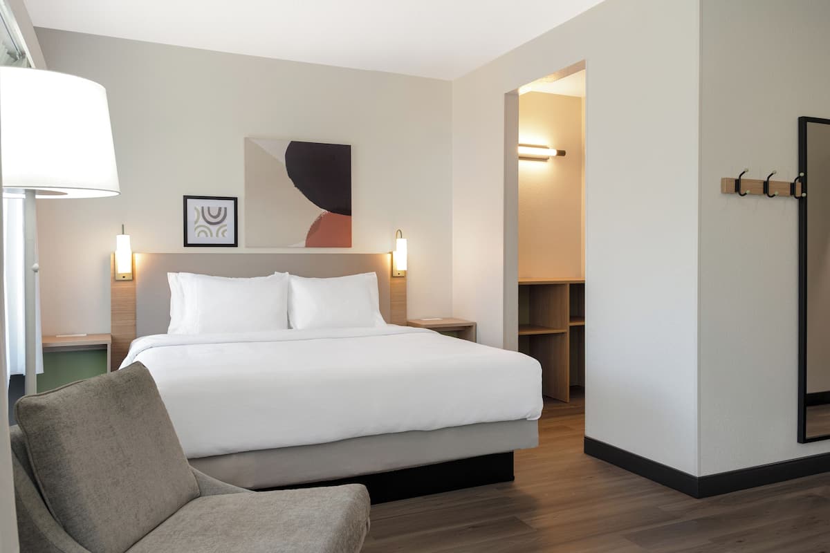 Een moderne hotelkamer met een groot bed, een bedlamp, een stoel en een tv aan de muur.