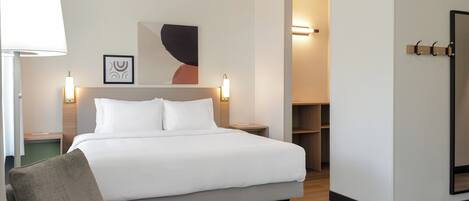 Una camera d'albergo moderna con un grande letto, una lampada da comodino, una sedia e una TV a parete.