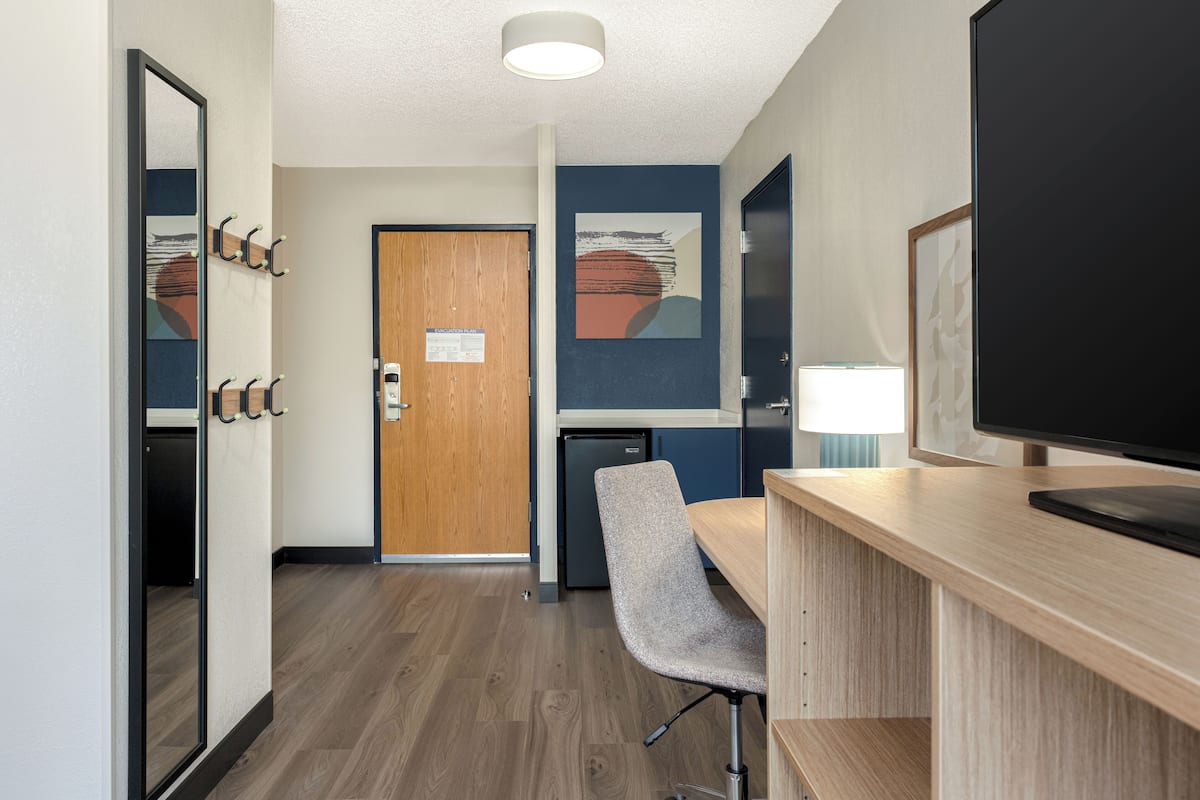Hotelkamer met een houten bureau, een stoel, een televisie, een kleine koelkast en een deur met een bordje.