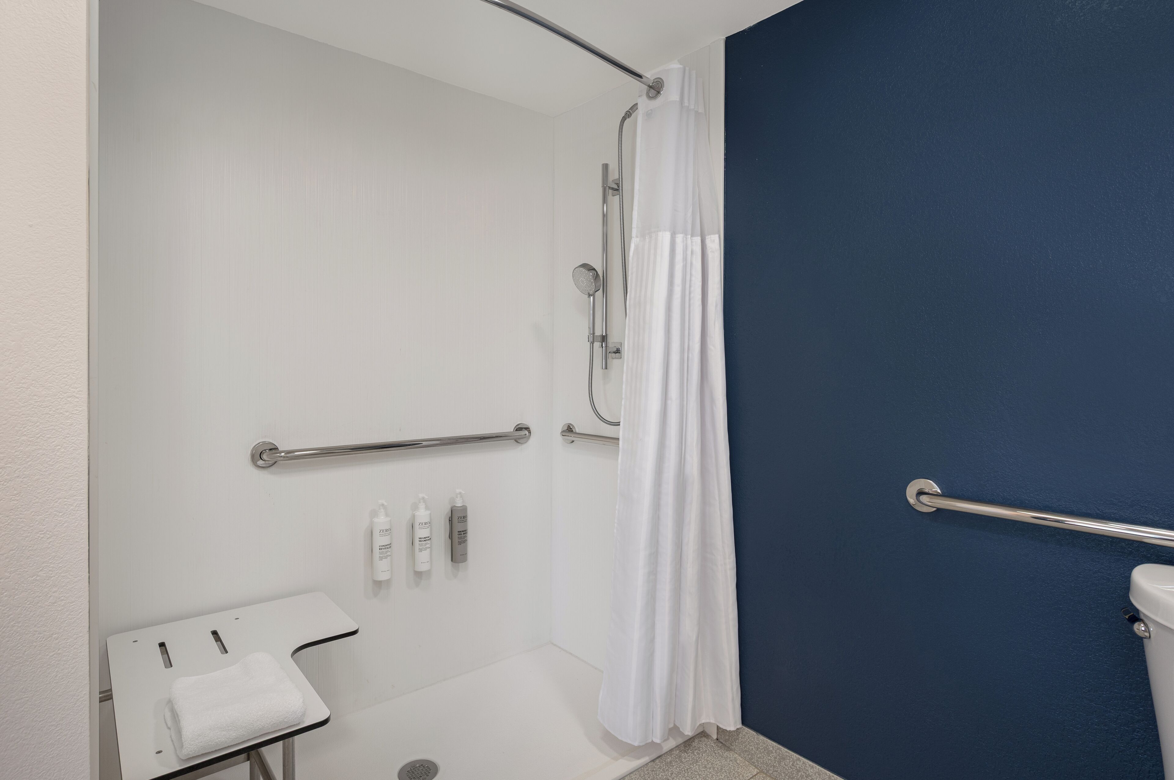 A bathroom with a white shower, a white sink with a towel, and a blue wall.