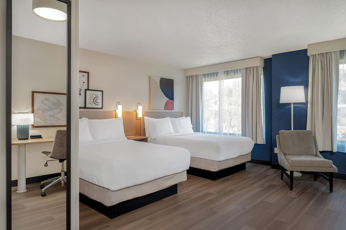 Een hotelkamer met twee bedden, een bureau met stoel, een lamp en kunst aan de muur.