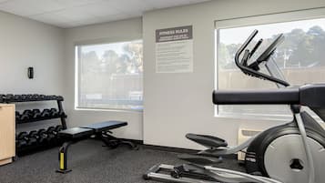 A gym with exercise equipment, a wall-mounted sign with fitness rules, and a window with a view of trees.