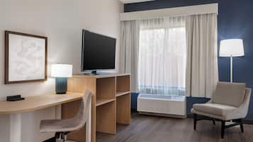 A hotel room with a desk, a chair, a television, a lamp, and a window with curtains.