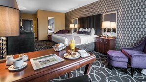 Habitación de hotel con cama, escritorio con productos de desayuno, una silla y pared con diseño.