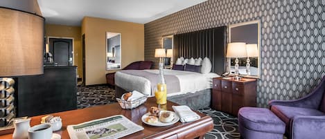 A hotel room with a bed, a desk with breakfast items, a chair, and a patterned wall.
