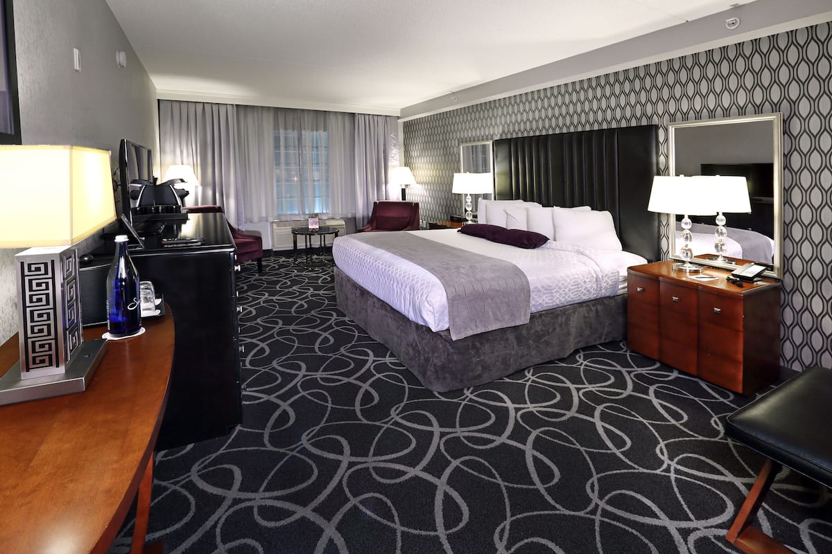 A hotel room with a large bed, a desk with a computer, a chair, and a dresser.