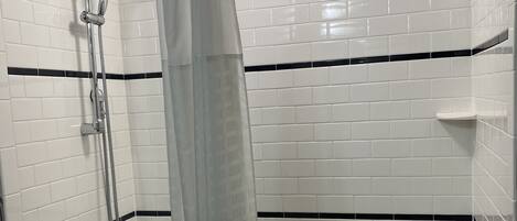A corner shower with white tiled walls, a showerhead, a handheld shower, and a curtain.