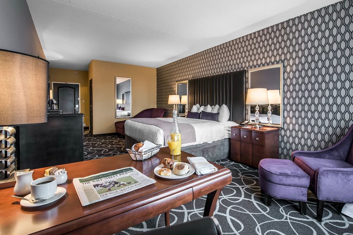 A hotel room with a bed, bedside table with a lamp, a desk with a chair, a coffee station, and a bathroom.
