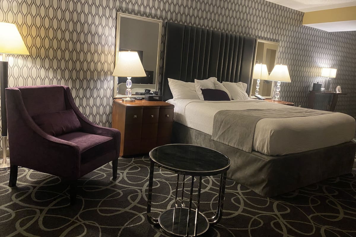 A hotel room with a bed, a chair, a small table, and a mirror.