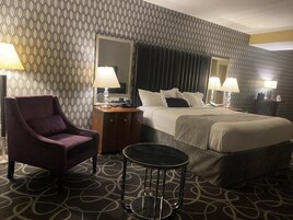 Una habitación de hotel con cama, una silla, una mesita y un espejo.