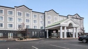 Un hotel de varios pisos con una entrada central, un estacionamiento y un cielo despejado.