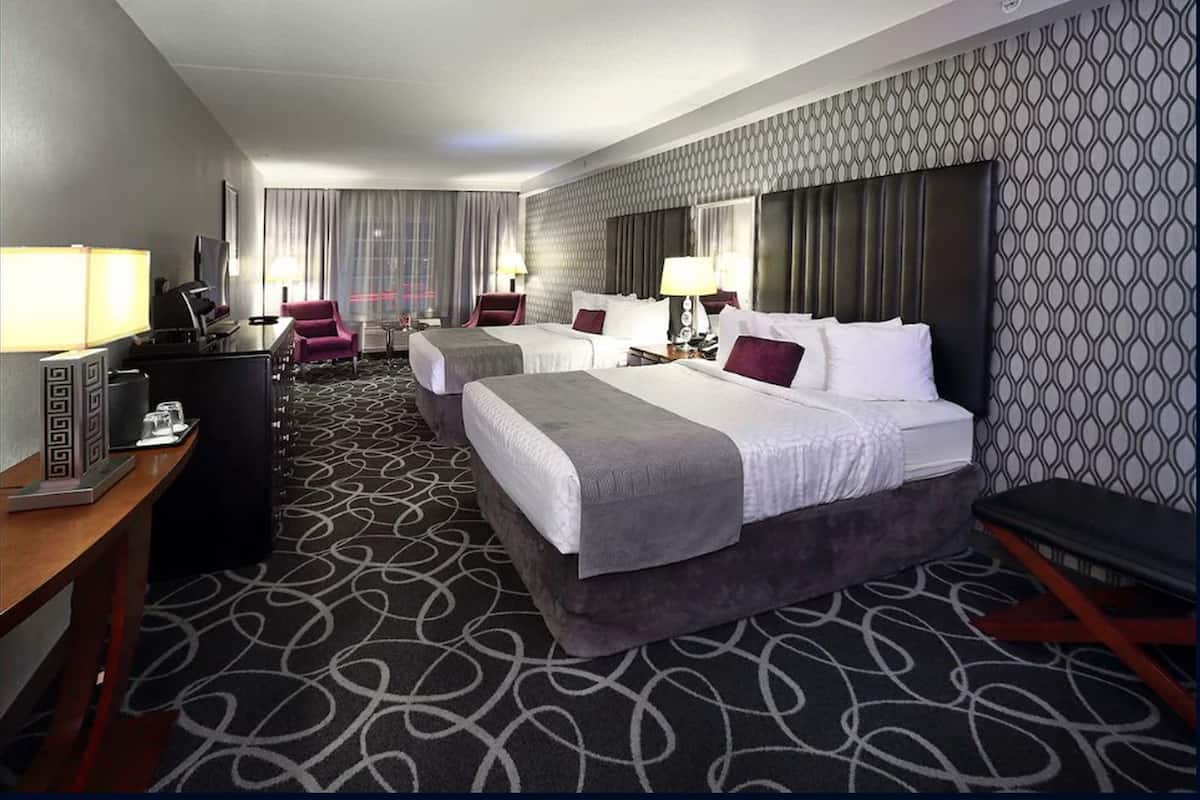 A hotel room with two beds, a desk, a chair, and a TV.