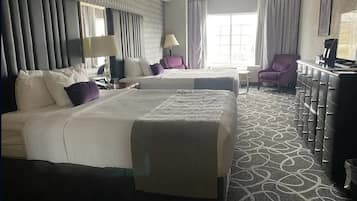A hotel room with two beds, a desk, a chair, a dresser, and a large window.