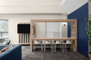 A modern office space with a long table, four chairs, a TV mounted on the wall, and a potted plant. - City Express By Marriott Redmond Bend Airport (Redmond)