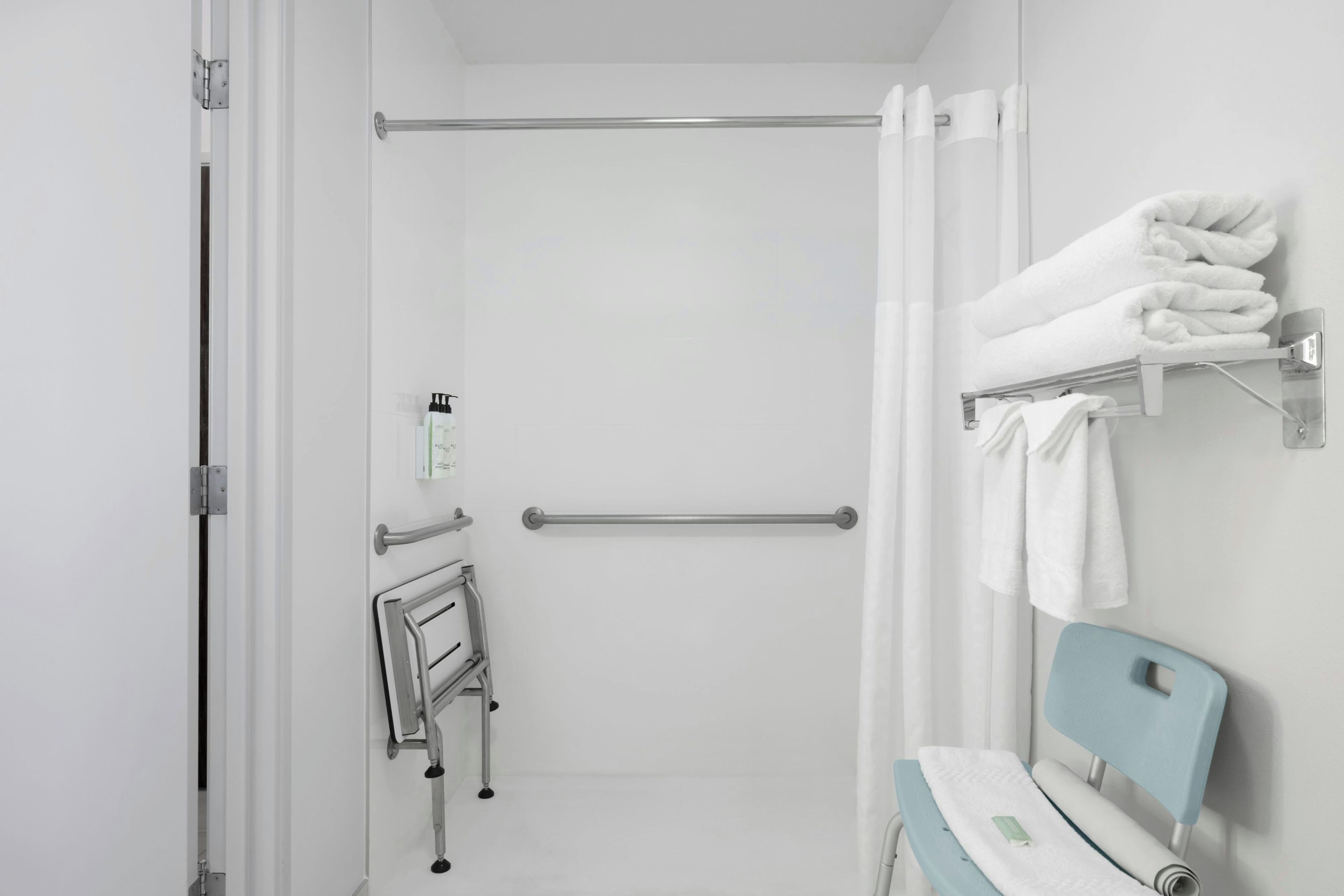 Baño con ducha, barandilla, barra de apoyo, toallero y banco accesible en silla de ruedas.