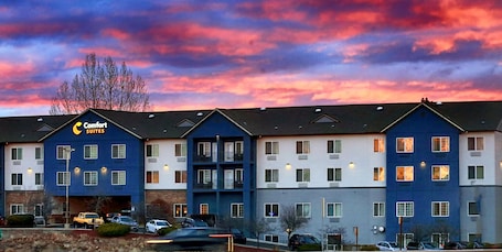 A hotel with multiple floors, a prominent 'Comfort Suites' sign, and a parking lot with several cars.