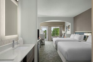 Habitación de hotel con una cama grande, una cama adicional, un escritorio con silla, un espejo amplio y una ventana con cortinas.