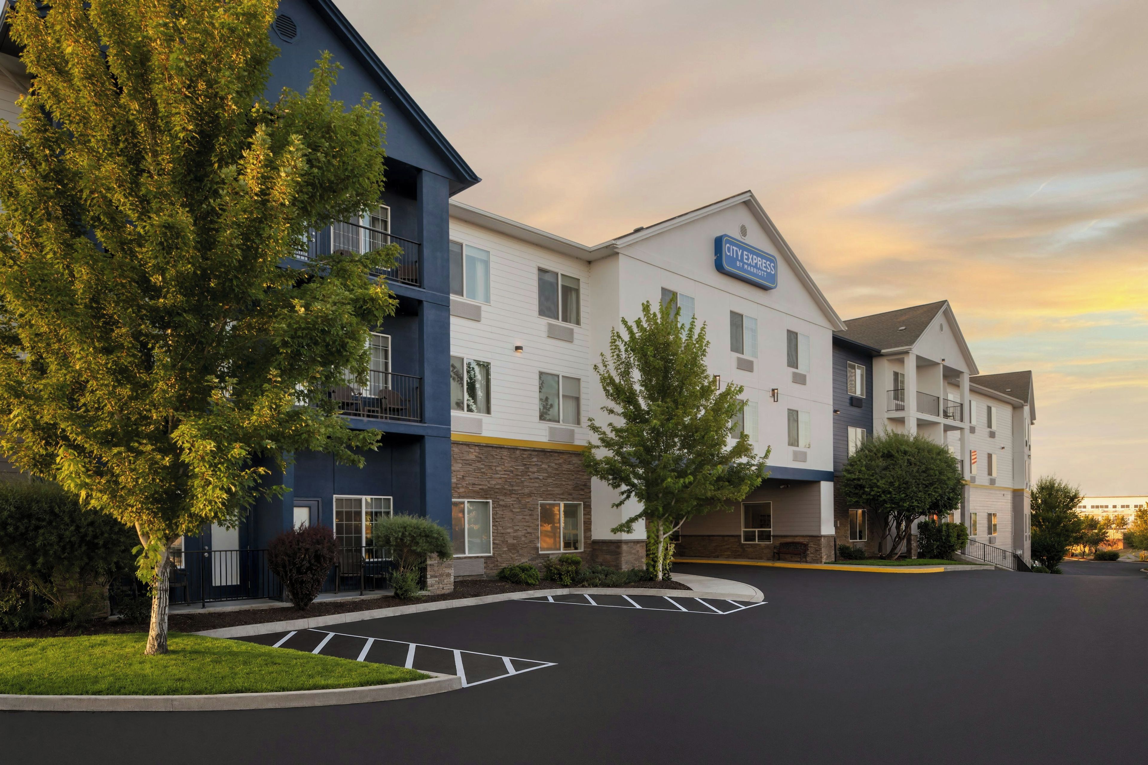 A multi-story hotel with a blue and white exterior, a parking lot, and a clear sky.