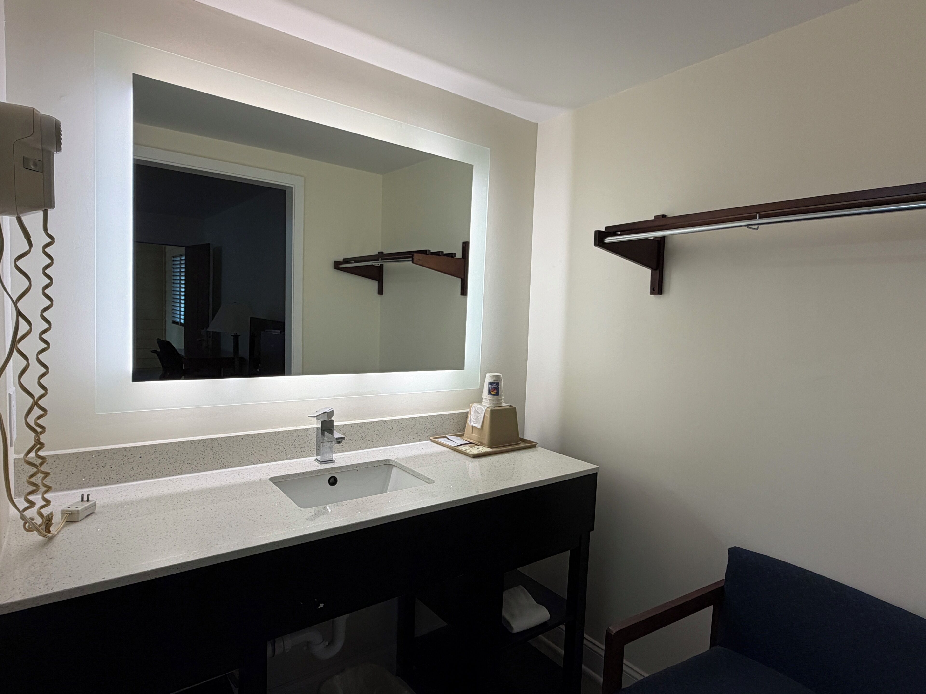 A bathroom with a large mirror, a sink, a towel rack, and a chair.