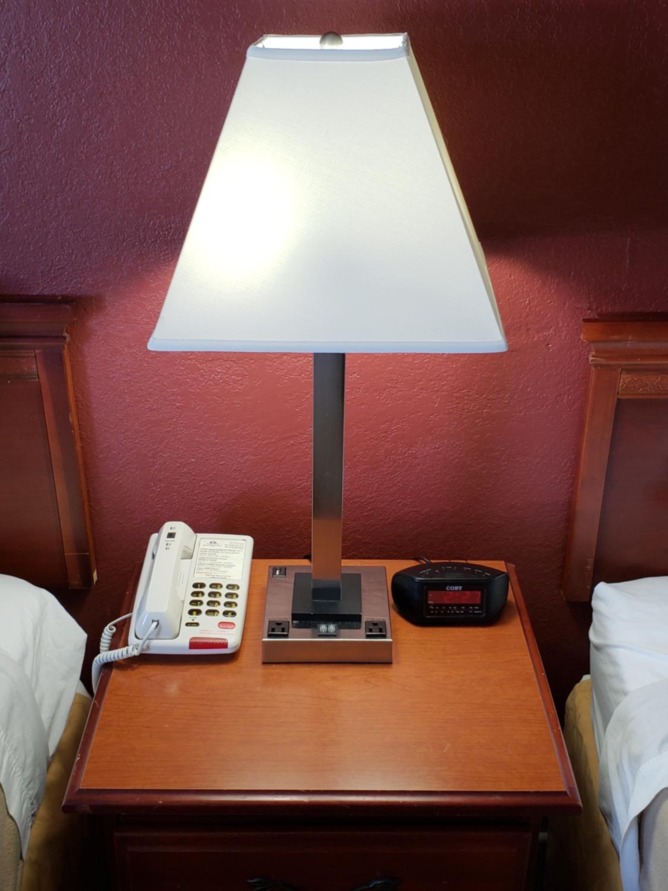 A hotel room with a bedside table, a lamp, a telephone, and a radio.