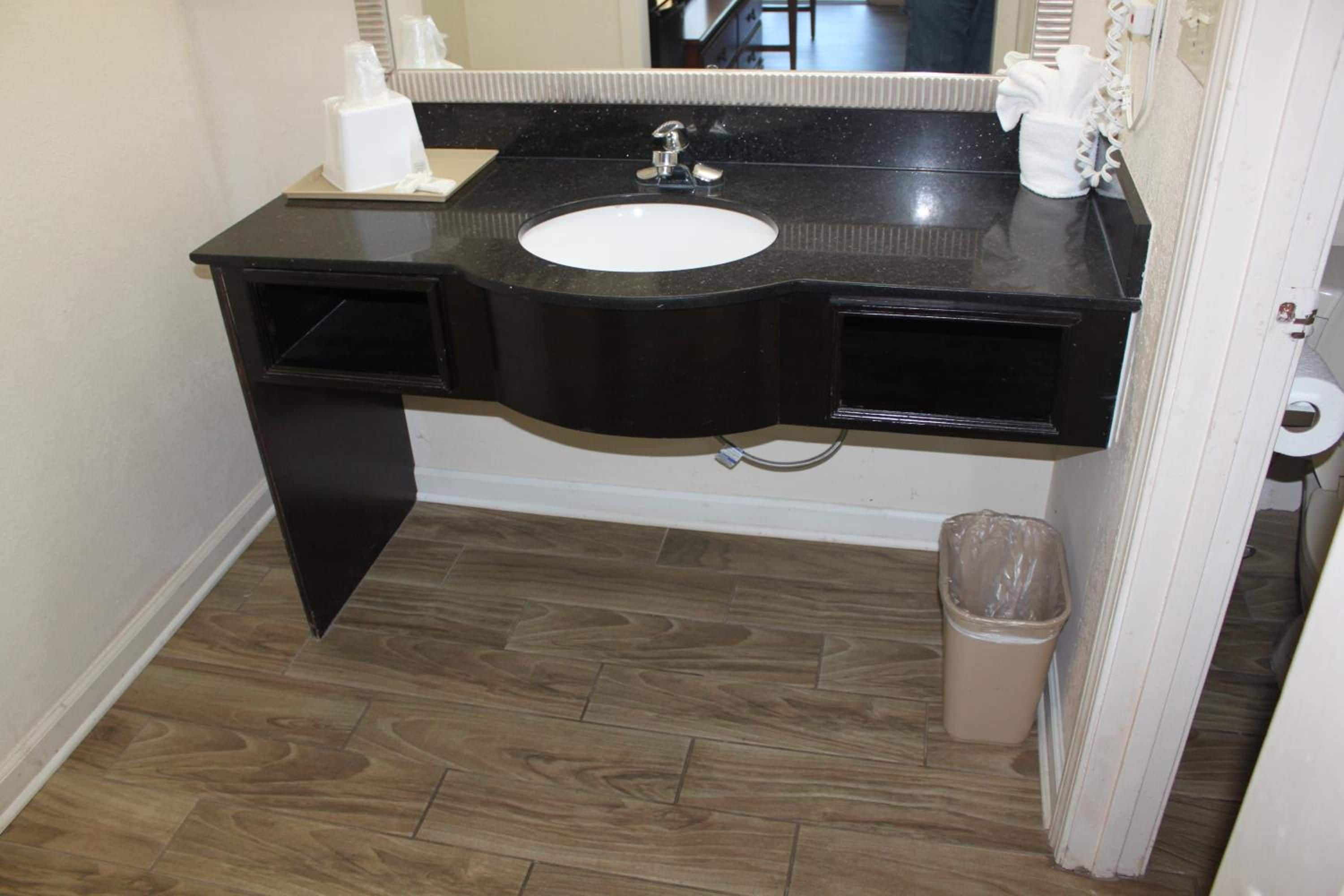 A bathroom with a black vanity, white sink, and a trash can.