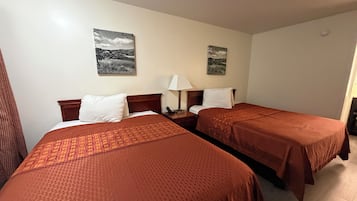 A hotel room with two beds, a nightstand with a lamp, and two wall-mounted pictures.