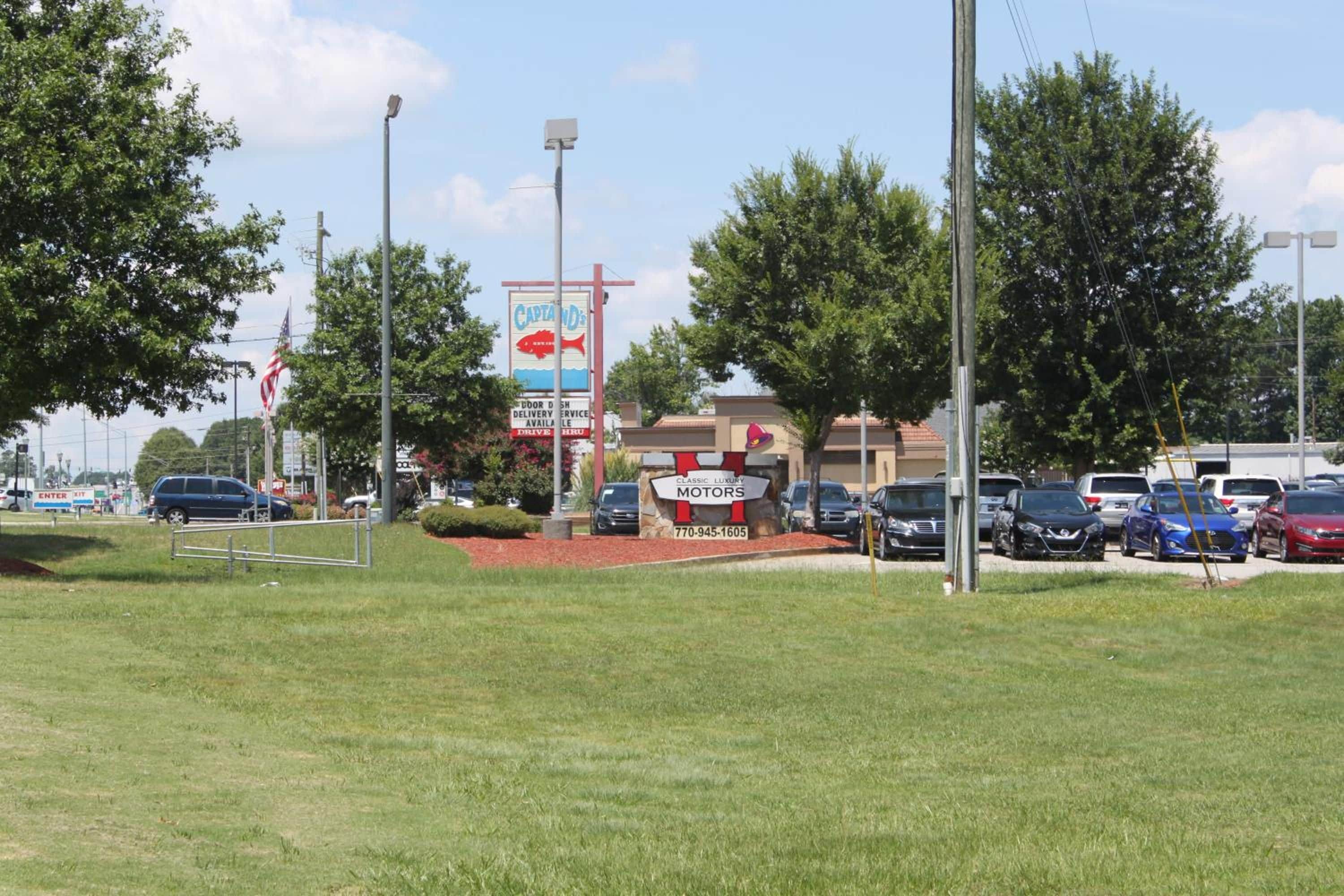 A parking lot with several cars, a building with a sign for 'Captain's Classic Luxury Motors', and a large billboard advertising a seafood restaurant.
