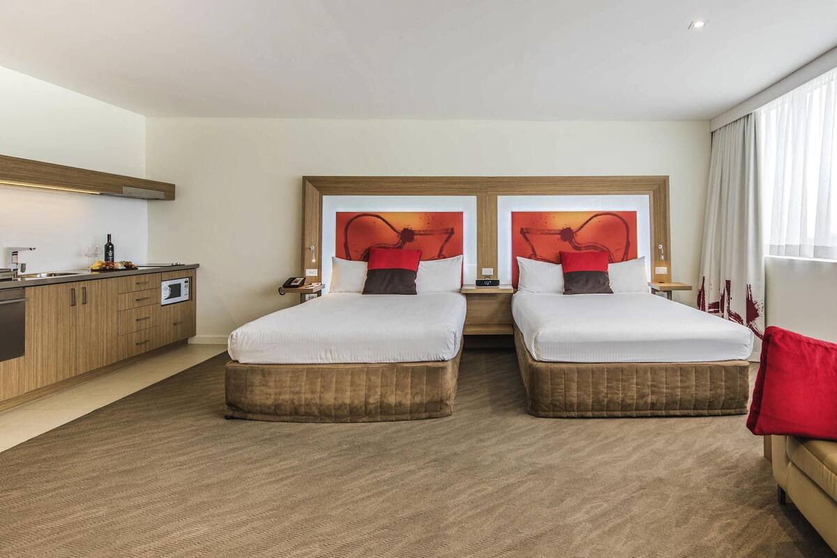 Una habitación de hotel con dos camas, kitchenette y un amplio ventanal.