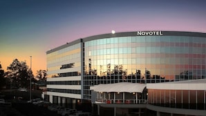 Un hôtel Novotel doté d’une façade incurvée et de grandes fenêtres qui reflètent le coucher de soleil.