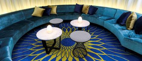 A cozy seating area with a blue sofa, two round tables with candles, and a patterned carpet.