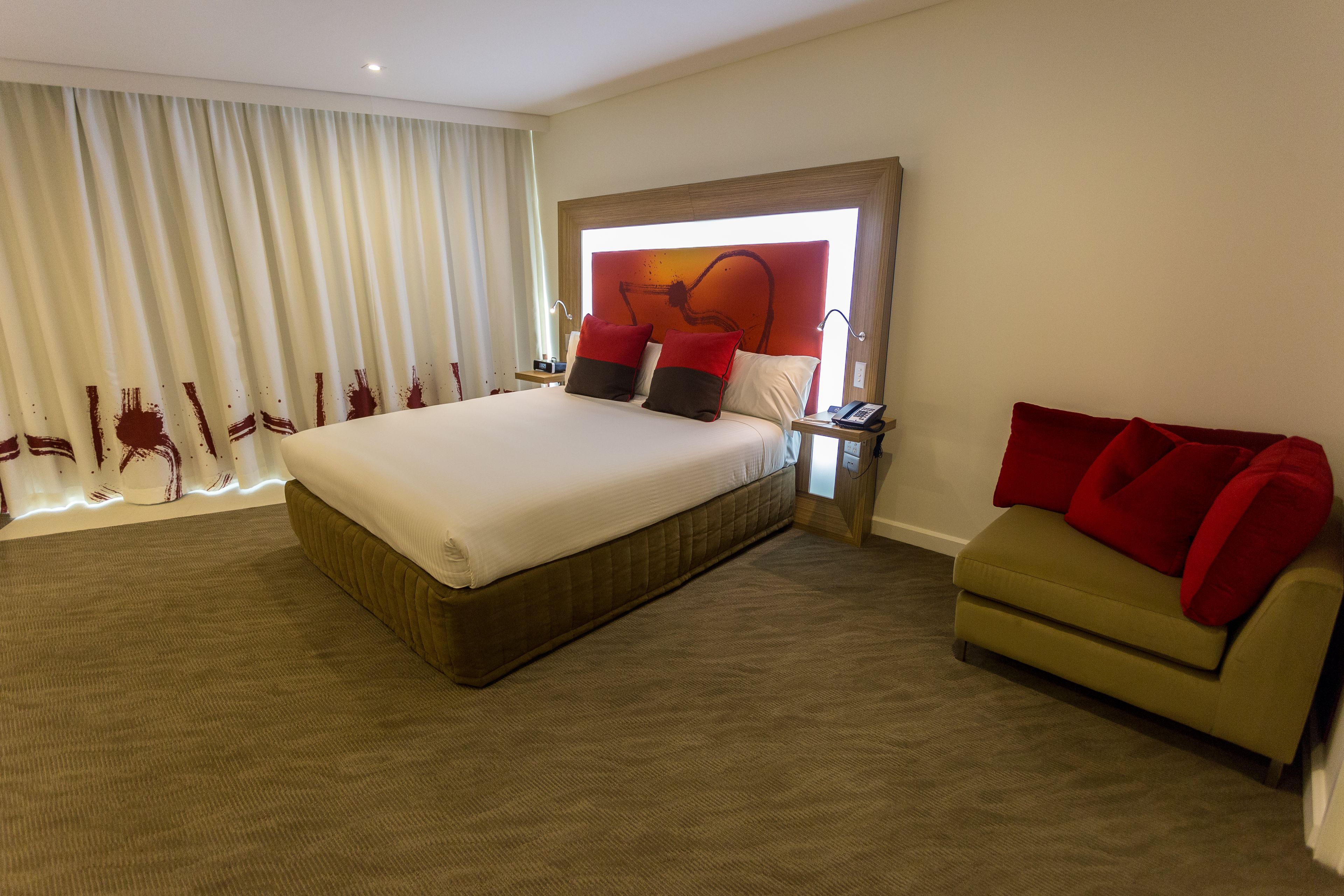 A hotel room with a large bed, a sofa, and a nightstand with a lamp.
