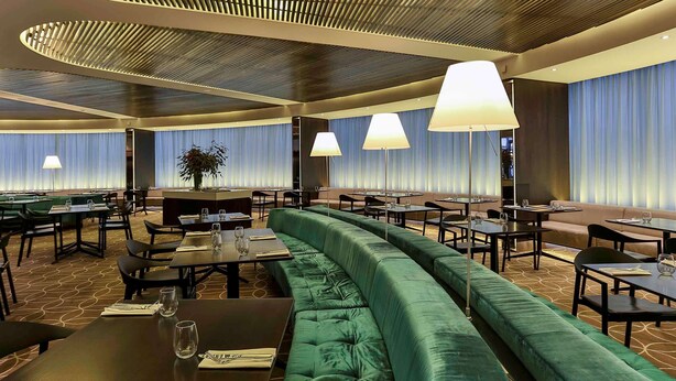 Un restaurant moderne avec un canapé recouvert d’un tissu vert, des tables et une lumière d’ambiance.