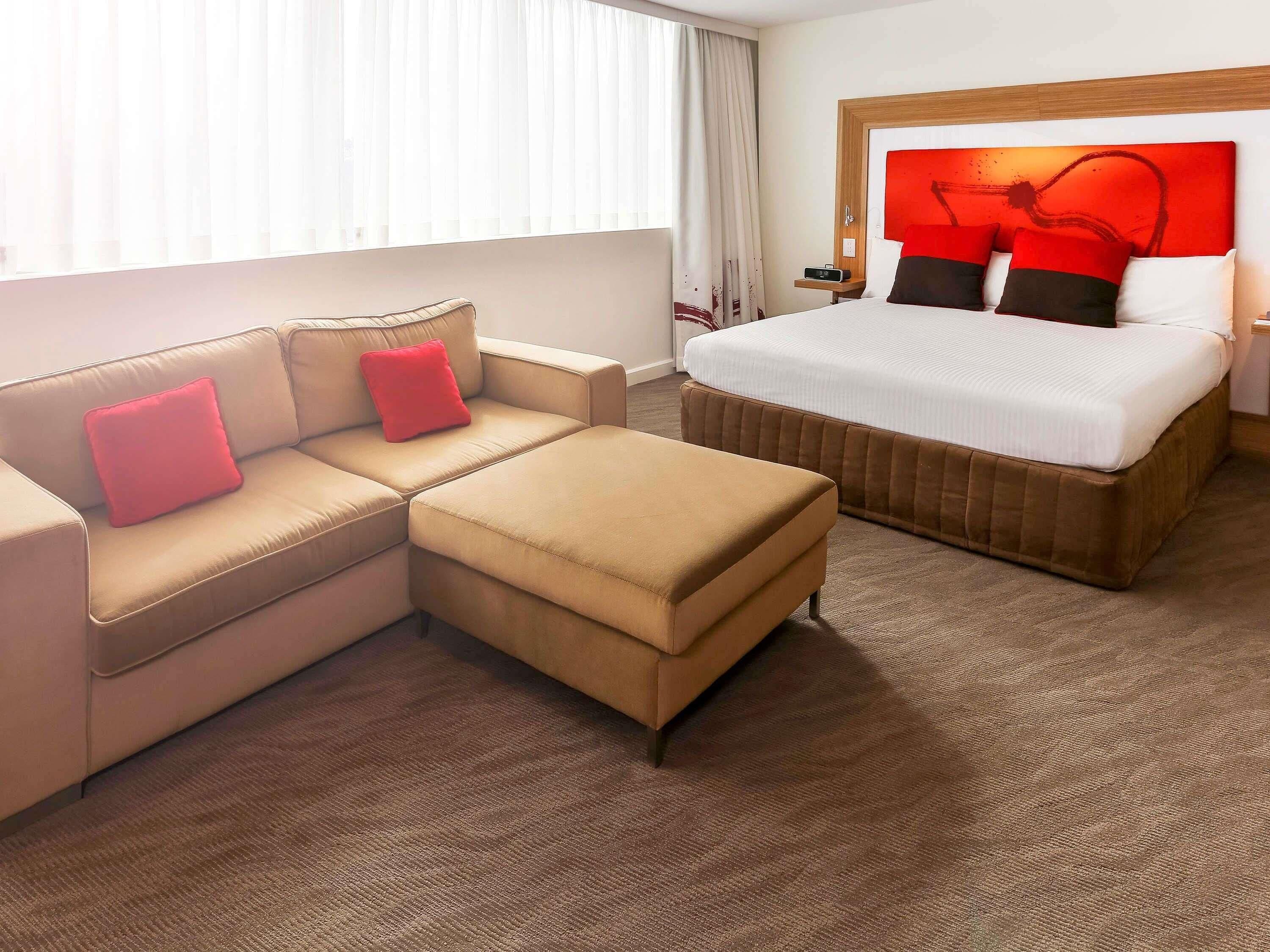 Una habitación de hotel con sofá, reposapiés y una cama con cabecera.