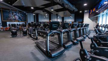 Un gimnasio con cintas de correr y bicicletas estáticas, un cartel de motivación grande y una pantalla digital en la pared.