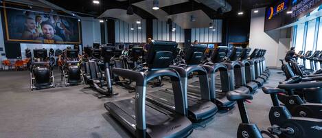 A gym with multiple treadmills and exercise bikes, a large motivational poster, and a digital display on the wall.