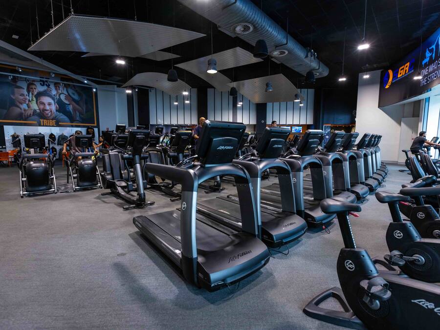 Un gimnasio con cintas de correr y bicicletas estáticas, un cartel de motivación grande y una pantalla digital en la pared.