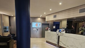 Un espace d’accueil d’hôtel avec un comptoir en marbre, une grande colonne et un écran numérique affichant des informations.