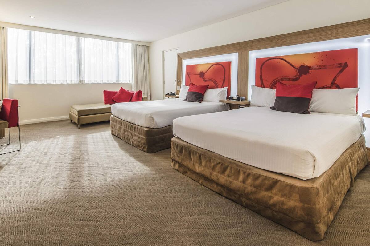 Habitación de hotel con dos camas, un sofá, un escritorio y un ventanal grande.