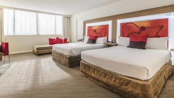 A hotel room with two beds, a sofa, a desk, and a large window.