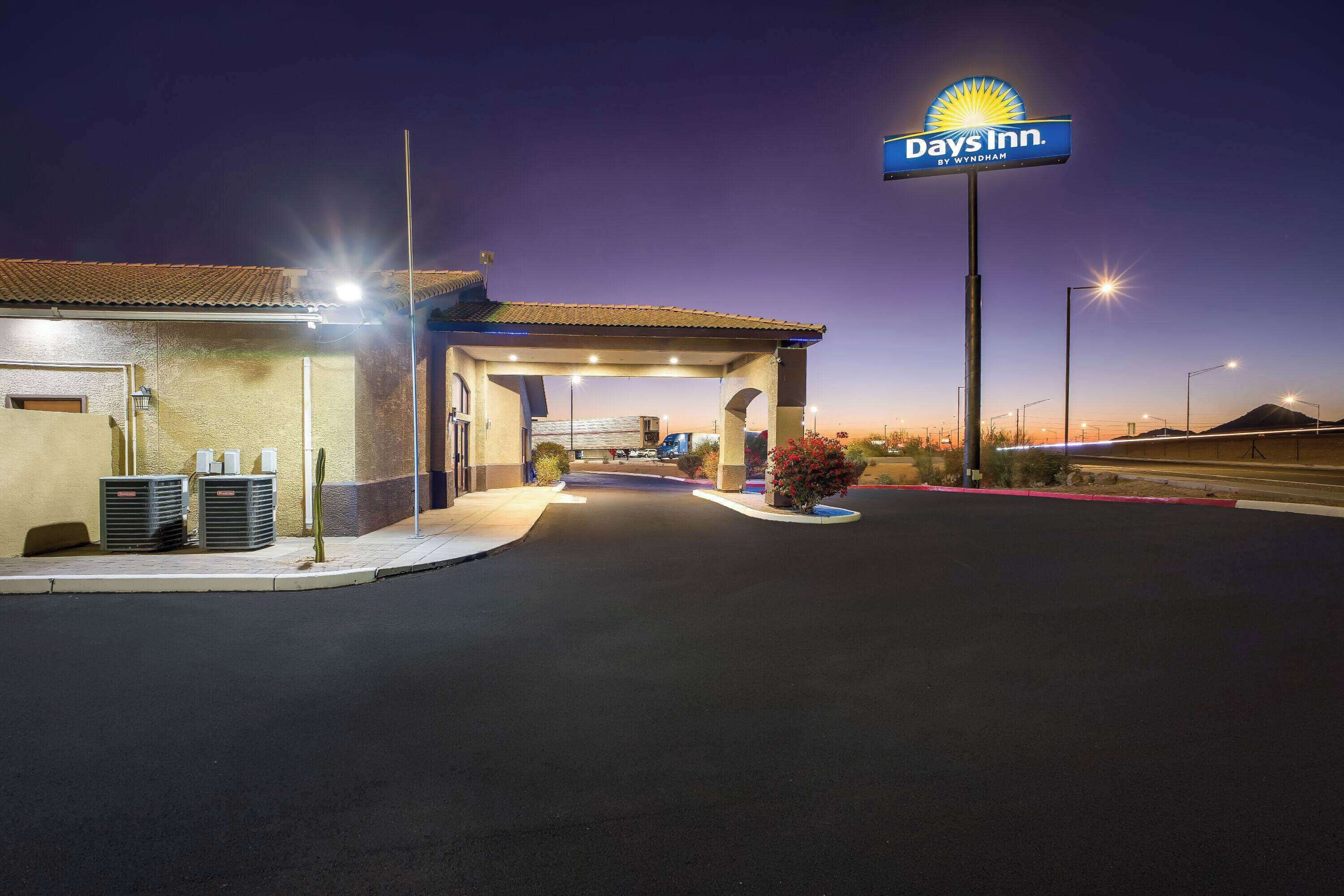 A Days Inn by Wyndham at dusk with a covered entrance, outdoor seating, and a clear sky.